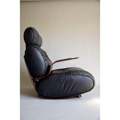 a black leather reclining chair with wooden legs and armrests in front of a white wall