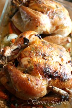 two whole chickens sitting on top of each other in a glass dish with carrots and onions