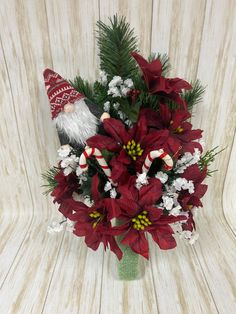 a vase filled with red and white flowers on top of a wooden table next to a wall