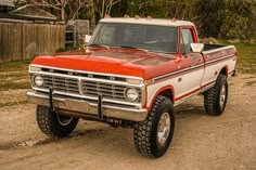 a red and white truck parked on top of a dirt road