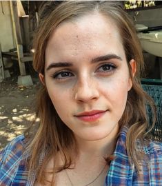 a young woman with freckled hair and blue eyes looks at the camera while wearing a plaid shirt