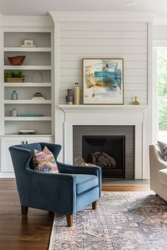 a blue chair sitting in front of a fire place next to a white book shelf