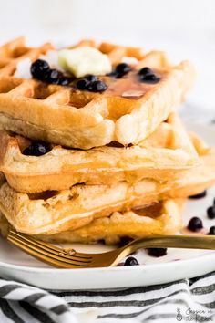 a stack of waffles with blueberries and butter on top sitting on a plate