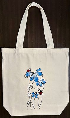 a white tote bag with blue flowers and ladybugs painted on the side