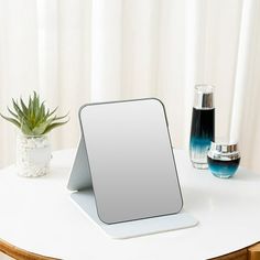 a mirror sitting on top of a white table next to a vase with a plant