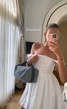 a woman taking a selfie in front of a mirror wearing a white off the shoulder dress