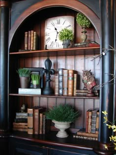 a bookshelf filled with lots of books next to a clock and potted plants