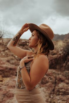 a woman wearing a brown hat and tan skirt standing in front of some rocky terrain