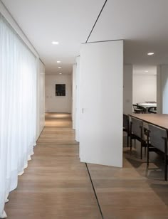 an empty room with white walls and wooden flooring, along with long tables and chairs