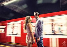 a man and woman standing in front of a red train at a subway station with motion blur