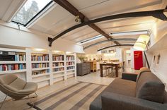 a living room filled with lots of furniture and bookshelves next to a kitchen