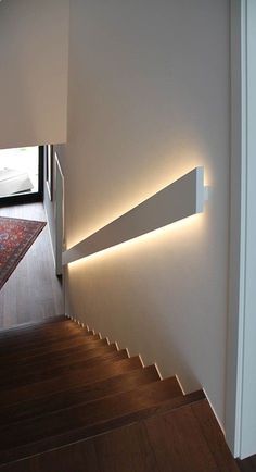 a white wall mounted light on the side of a wooden floor next to a stair case