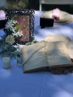 an open book sitting on top of a table next to a candle and some flowers