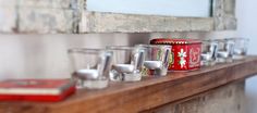 several shot glasses are lined up on a wooden shelf next to a book and mirror