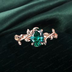 an emerald colored ring with leaves and vines on the side, sitting on a green velvet surface