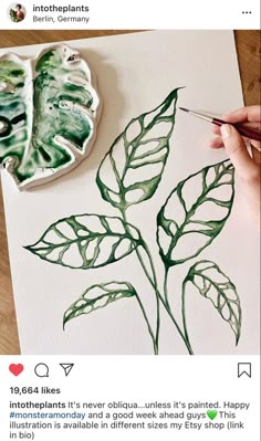 a person is painting a green leaf on a piece of paper with watercolor pencils