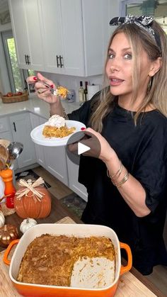 a woman holding a plate with food in it on a kitchen counter next to pumpkins