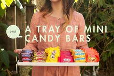 a woman holding a tray with candy bars on it and the words, a tray of mini candy bars