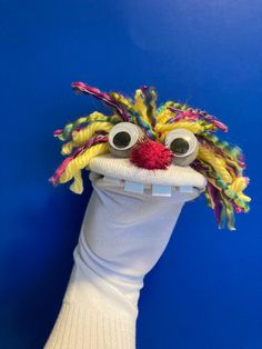 a knitted puppet head with big eyes and colorful hair on it's face