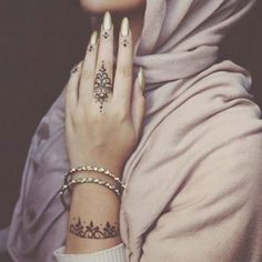 a woman wearing a hijab with tattoos on her arm and hand is shown