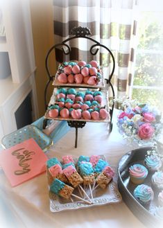 a table topped with cakes and cupcakes covered in frosting next to a window