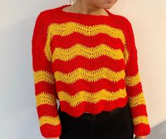 a woman wearing a red and yellow knitted sweater standing in front of a white wall