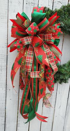 a christmas wreath hanging on the side of a white fence with red and green ribbons