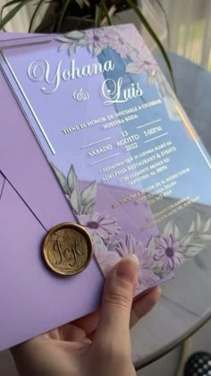 a person holding up a purple and silver wedding card with a gold coin on it