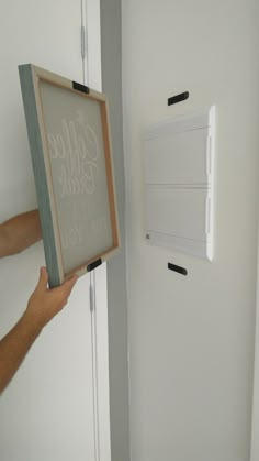 a person holding up a framed sign in front of a wall mounted light switch box