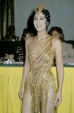 a woman in a gold dress standing next to a table