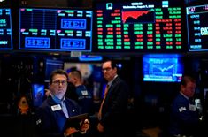 a man standing in front of an array of stock market screens and trading information on the wall street