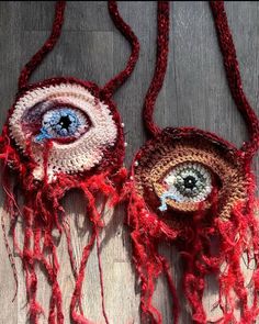 two crocheted evil eye purses hanging on a wooden floor with red yarn