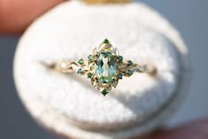 a close up of a person holding an engagement ring with green and white stones on it