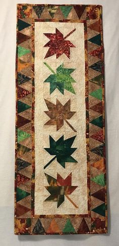 a quilted wall hanging with leaves on it's sides and an arrow in the middle