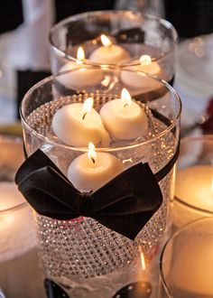 candles are arranged in glass bowls with black bow ties on the top and bottom, along with other lit candles