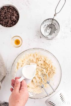 someone mixing ingredients in a glass bowl with a whisk on the side and chocolate chips next to it