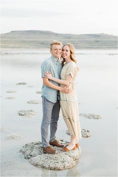 a man and woman standing on rocks in the water with their arms around each other