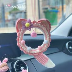 a car dashboard with a pink and white knitted steering wheel cover hanging from it's center console