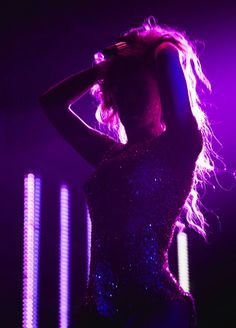 a woman with long hair standing in front of purple lights