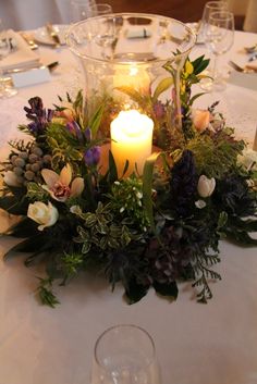 a candle is lit on a table with flowers and greenery