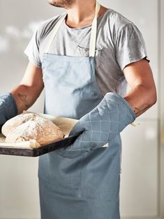 a man in an apron is holding a tray with bread on it and wearing gloves