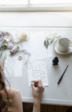 a woman is writing on paper at a table with flowers and other items around her