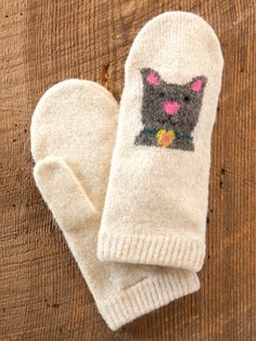 a pair of white mittens with a black cat on it sitting on top of a wooden table