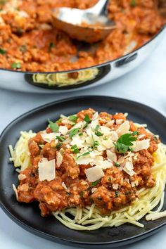 two plates of spaghetti with meat sauce and parmesan cheese on top, next to a skillet