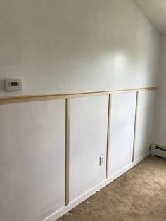 an empty room with white walls and wood paneling on the wall, in front of a heater