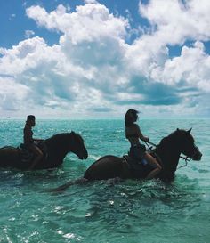 two people riding horses through the ocean on a sunny day with blue skies and white clouds