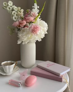 a white table topped with a vase filled with flowers next to a cup of coffee