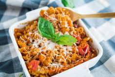 a casserole dish filled with pasta, cheese and basil garnished with parmesan cheese