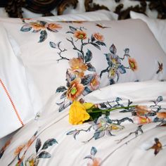 a yellow flower laying on top of a bed next to pillows and pillowcases