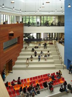 people are sitting on red chairs in the middle of a large room with stairs and windows